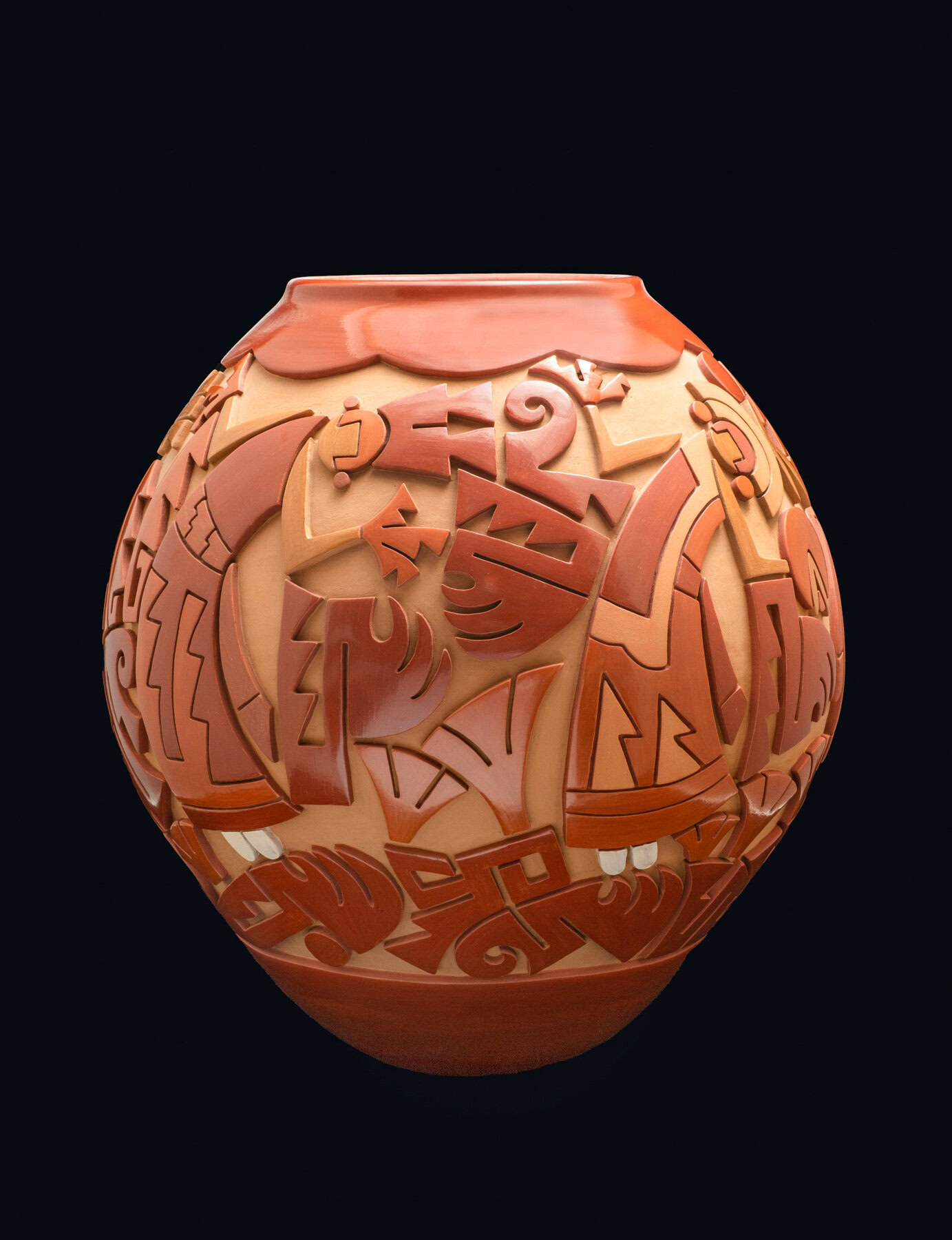 A rounded, reddish-brown pottery vase with intricately carved and painted designs in a mix of darker red-orange tones, set against a black backdrop.